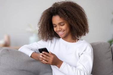 Gülümseyen Afrikalı genç kız akıllı telefon kullanarak arkadaşlarıyla internette sohbet ediyor.