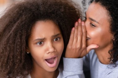 Shocked african daughter listening to black mom whispering in ear clipart