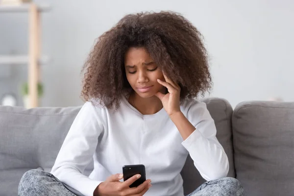 Upset depressed african teen girl looking at phone at home — Stock Photo, Image