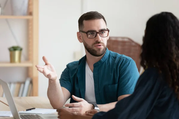 Thoughtful young businessman in glasses discussing project with biracial colleague. — Stock Photo, Image