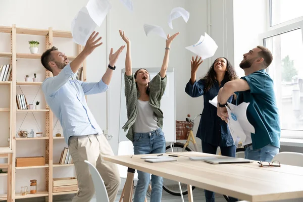 Alegre joven equipo de negocios multirracial lanzando documentos de papel en el aire . — Foto de Stock