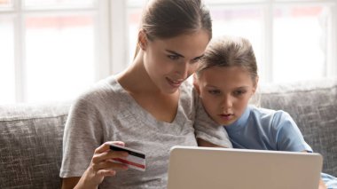 Kafadan çekilen portre konsantre olmuş genç anne ve kızı online alışveriş yapıyor..