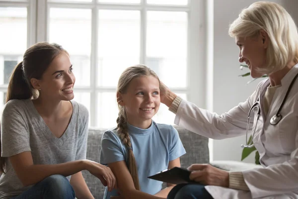 Middle aged female pediatrician stroking head of smiling school girl. — Stock Photo, Image