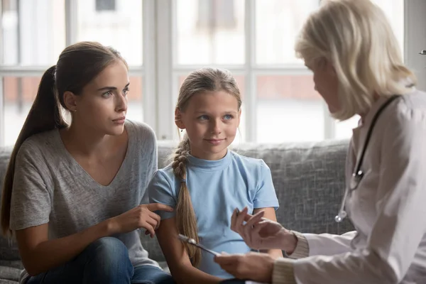 Serious young mother with school daughter attending mature pediatrician. — Stock Photo, Image