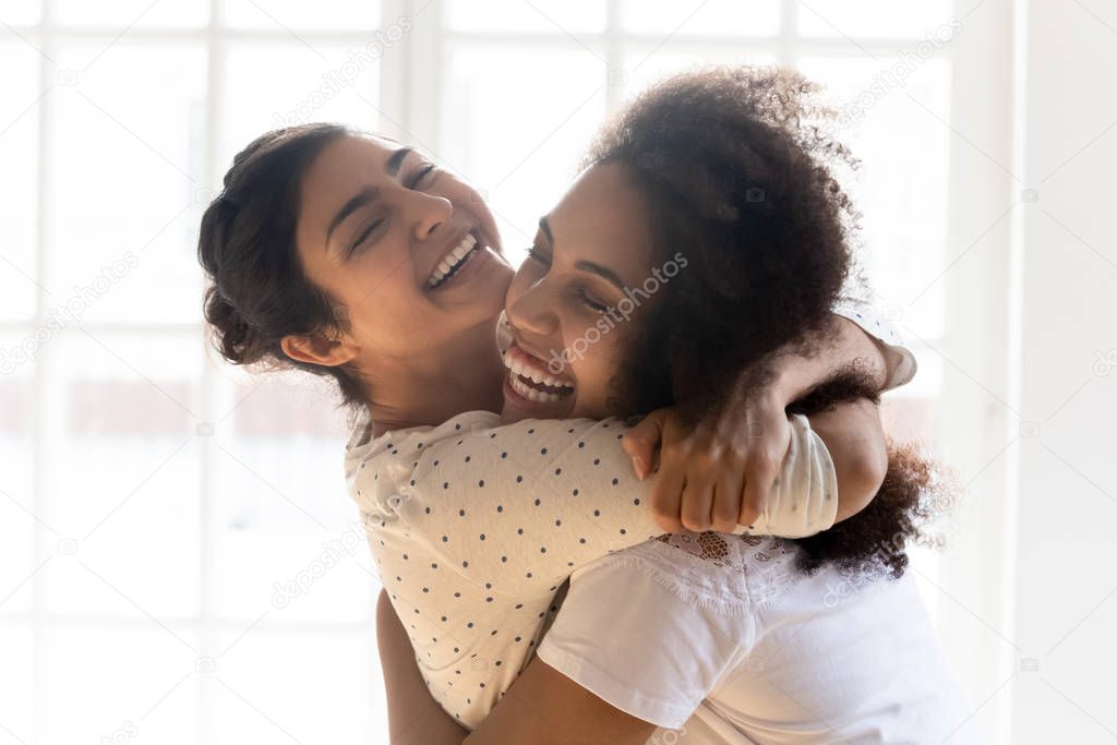 Happy Indian and African ethnicity friends cuddle each other indoors