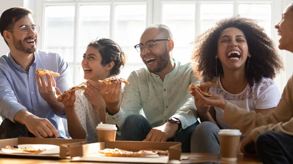 Riendo amigos multi raciales comiendo pizza en el interior — Foto de Stock