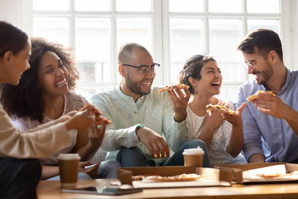 Cinco amigos multiétnicos riendo comiendo pizza en el interior — Foto de Stock