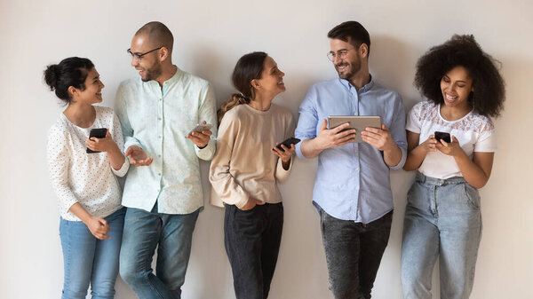 Веселые друзья с разнообразным современным гаджетом, позирующим в помещении
