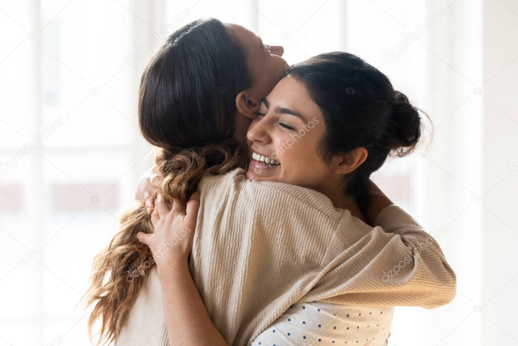 Candid multiracial girls best friends embracing standing indoors