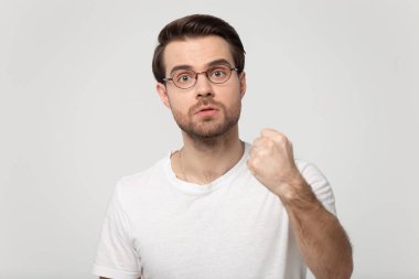 Gözlüklü agresif genç adam yumruğunu sıkıyor, gücünü gösteriyor..