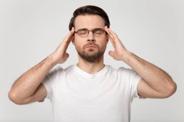 Stressed young guy in eyeglasses suffering from headache.