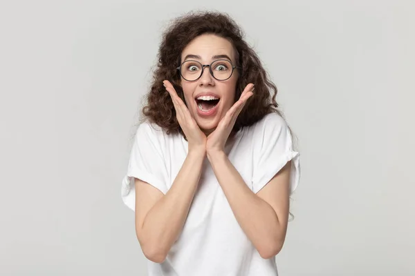 Happy girl in eyeglasses holding hands near cheeks, shouting. — Stockfoto