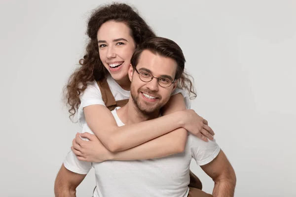 Young man in eyeglasses giving piggyback ride to happy attractive woman. — Zdjęcie stockowe