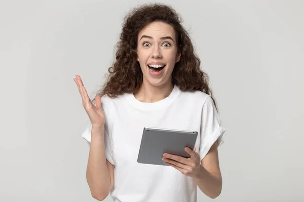 Amazed millennial girl holding digital tablet in hands, feeling joyful. — Stockfoto