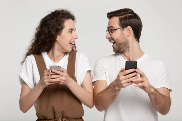 Excited amazed young couple looking at each other, holding cellphones. — 스톡 사진