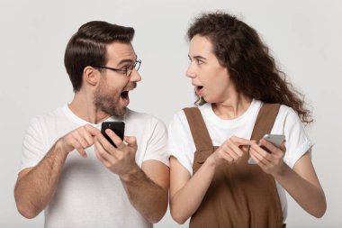 Astonished happy young couple holding mobile phones, pointing at screen.