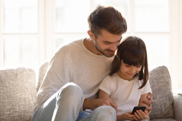 Genç baba, küçük kızıyla akıllı telefon kullanarak rahatlıyor. — Stok fotoğraf