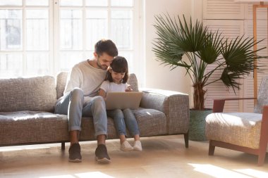 Mutlu genç baba anaokulu kızıyla dizüstü bilgisayar kullanarak rahatlıyor.