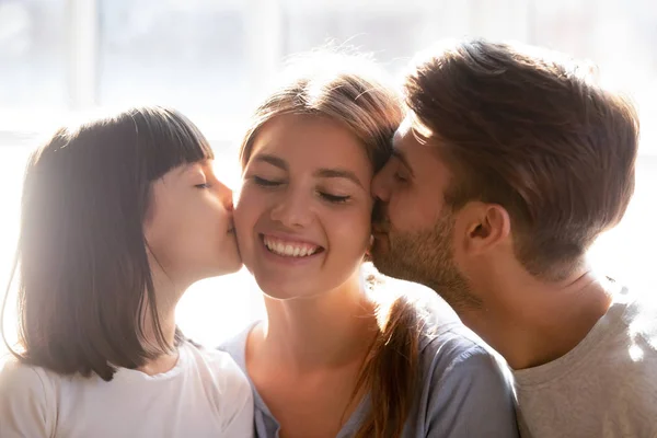 Любящий папа и маленькая дочь целуют улыбающуюся маму в щеки — стоковое фото