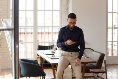 Modern ofis odasında akıllı telefonu olan Orta Doğulu bir iş adamı.