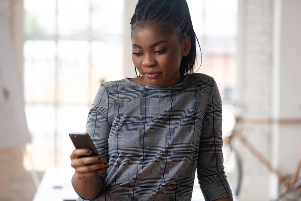 African woman holding smartphone looking at screen at work-place — Stock Photo, Image