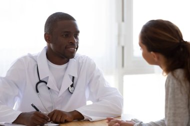 Smiling African American doctor listening to female patient in clinic