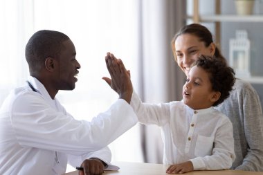 Friendly African American pediatrician doctor giving five to little boy