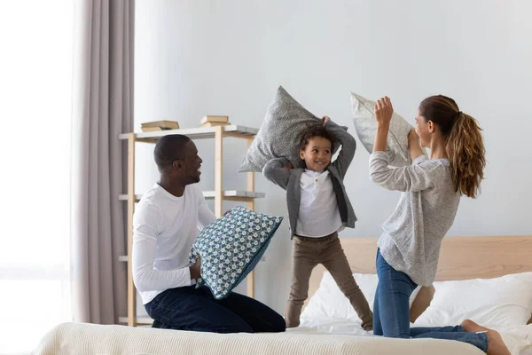 Feliz familia afroamericana jugando lucha de almohadas en la cama —  Fotos de Stock