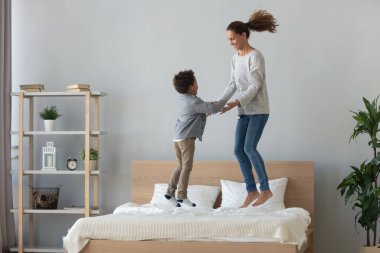 Happy mixed race mother and little son jumping on bed