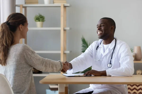 Smiling African American doctor shaking hand of female patient — Stock Fotó