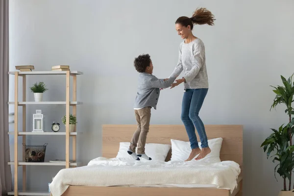Feliz madre de raza mixta e hijo pequeño saltando en la cama —  Fotos de Stock