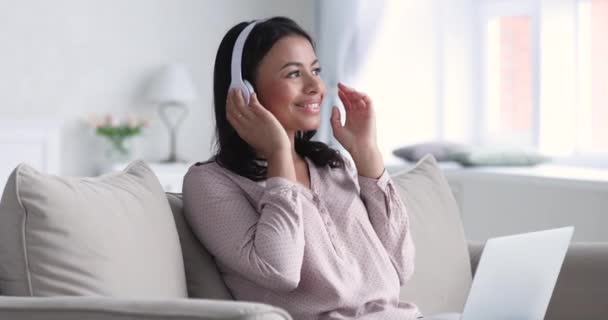 Smiling african woman wear headphones using laptop sit on sofa — Stockvideo