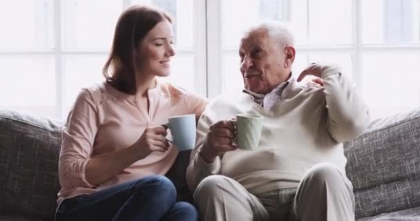 Feliz abuelo y nieta hablando de beber té sentarse en el sofá — Vídeo de stock