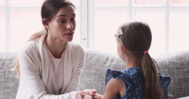 Önemseyen genç anne el ele tutuşup küçük kızla konuşuyor.