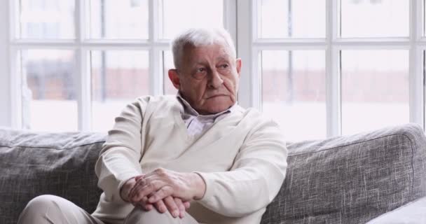 Pensive lonely older grandfather sitting alone on couch looking away — Stock video