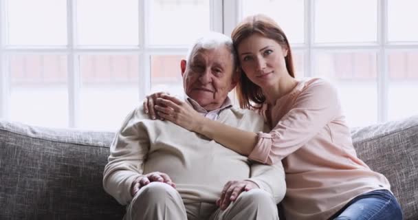 Feliz joven nieta abrazando viejo abuelo sentarse en sofá, retrato — Vídeo de stock