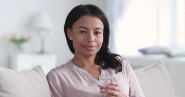 Gülümseyen Afrikalı kadın bir bardak su tutarak baş parmağını kaldırıyor.