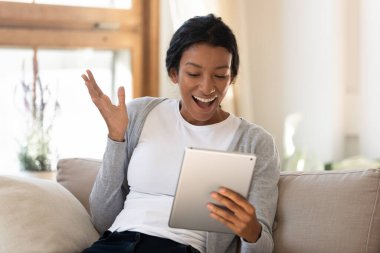 Excited african American woman shocked by online news on tablet