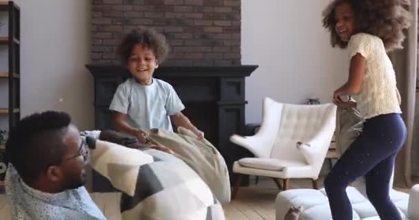 Réjoui afro-américain petit frère soeur combattant papa avec des oreillers . — Video