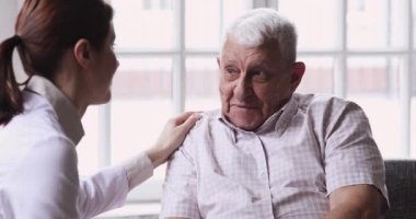 Bayan doktor bakıcı, tıbbi ziyaret sırasında büyükbaba hastaya destek oluyor.