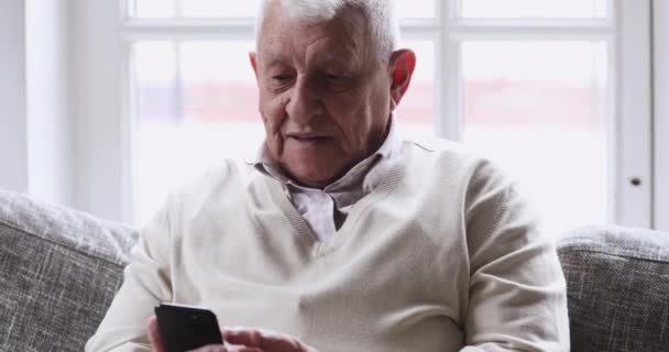 Feliz hombre mayor utilizando el teléfono inteligente relajarse en el sofá — Vídeos de Stock