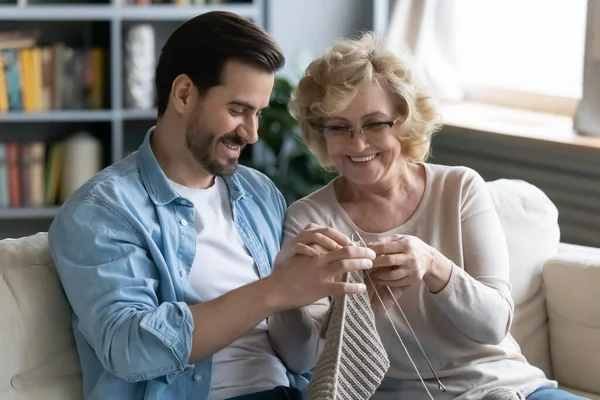 Happy senior mother teach knitting adult son