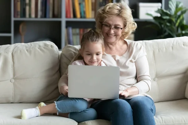 Sorrindo sênior anos 60 vovó usar laptop com neta pequena — Fotografia de Stock