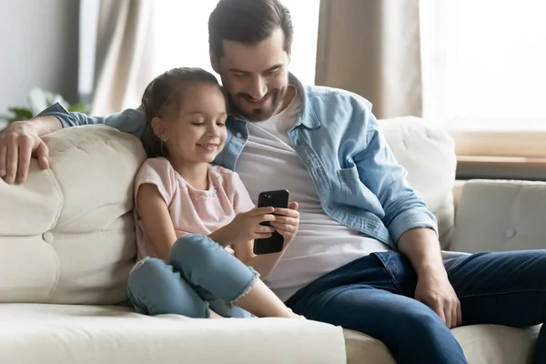 Jovem pai relaxar com a pequena filha usando célula — Fotografia de Stock