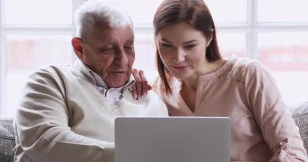 Glimlachend jong volwassen volwassen kleindochter onderwijzen oude grootvader met behulp van laptop — Stockvideo