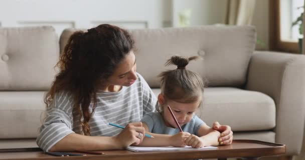 Ευχάριστη γυναίκα δασκάλα ζωγραφίζει εικόνες σε άλμπουμ με κοριτσάκι. — Αρχείο Βίντεο