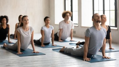 Erkek eğitmen ve bir grup insan Upward Facing Dog 'u oynuyorlar.