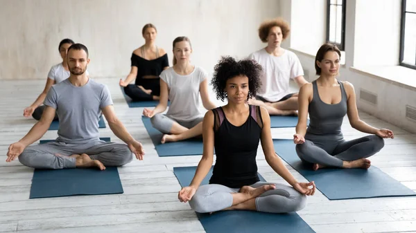 Různí mladí lidé seděli se zkříženýma nohama cvičení meditace společně uvnitř — Stock fotografie
