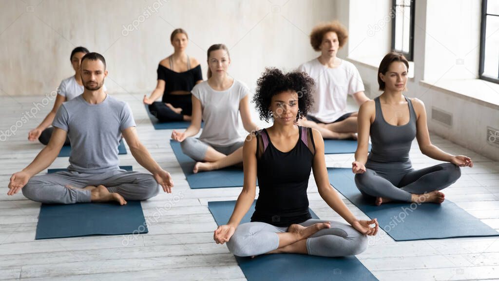 Diverse young people seated cross-legged practicing meditation together indoors