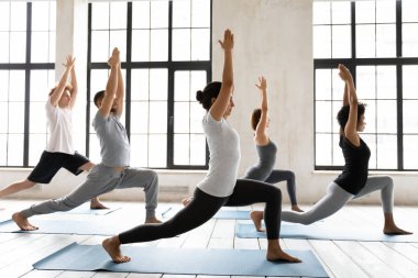 Warrior One ya da Virabhadrasana 'daki insanlar spor stüdyosunda poz veriyorlar.
